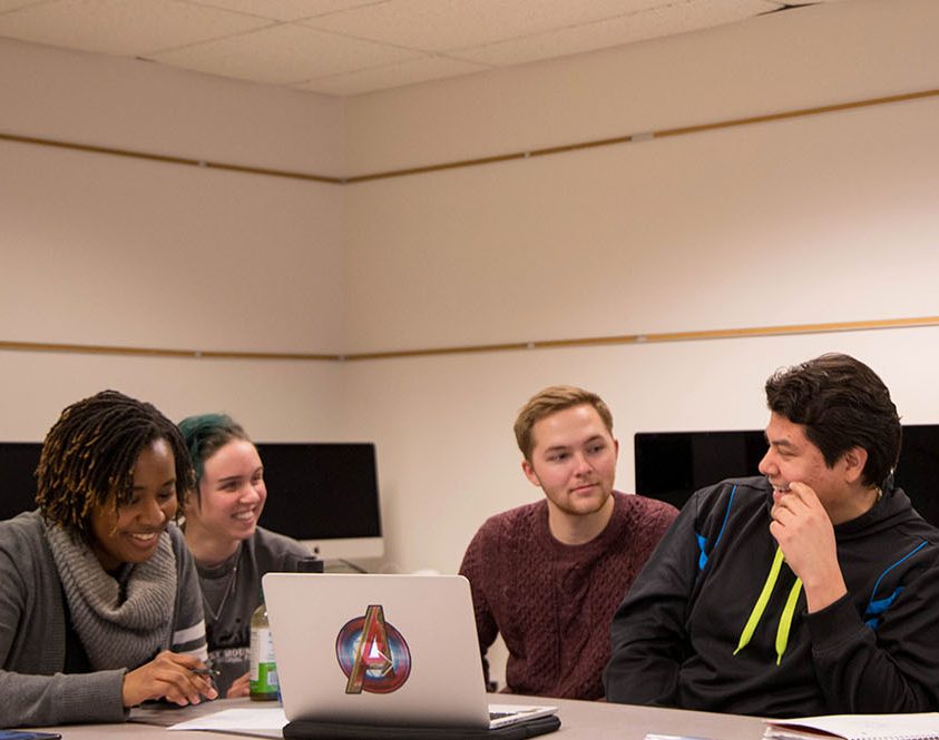 Three female and three male students meet in a computer lab around a computer.