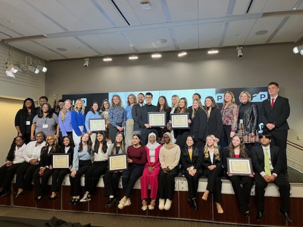 Large group of students pose on stage holding their plaques.