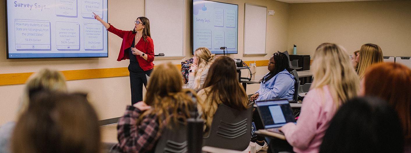 A faculty member teaches a class as students take notes on laptops