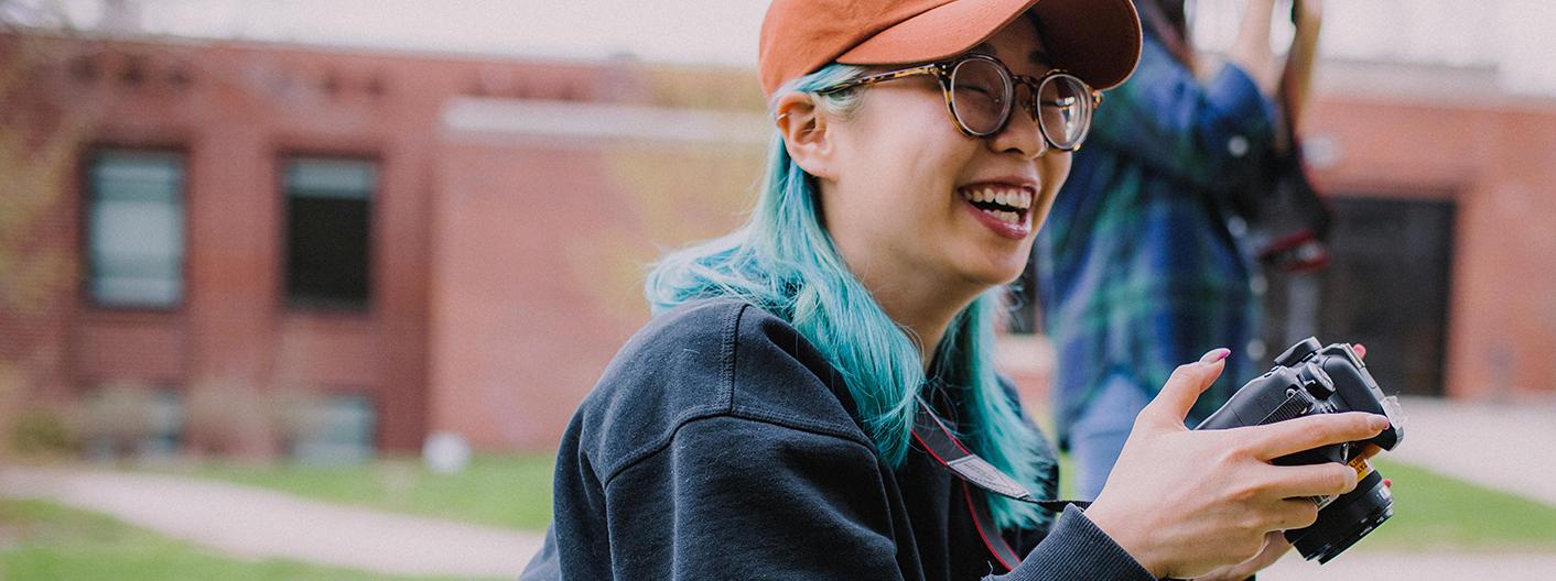 A Greenlee student smiles while adjusting camera settings outside Hamilton Hall